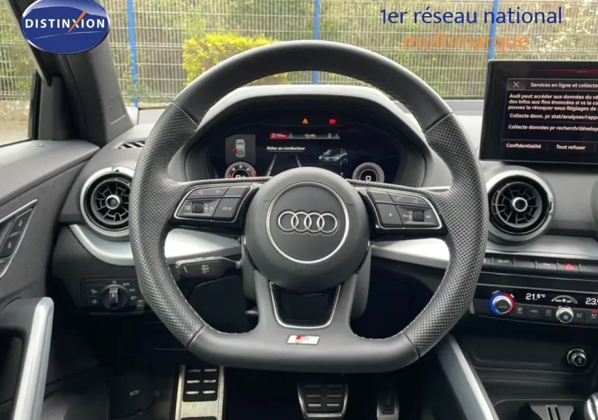 Vue intérieure centrée sur le volant noir perforé de l'Audi Q2 35 2.0 TDI S-Line avec tableau de bord digital et aérateurs ronds.