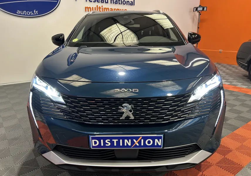 Vue avant frontale du Peugeot 5008 bleu Célèbes avec calandre noire et phares LED allumés en showroom.