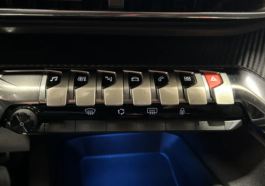 Gros plan sur la rangée de commandes métalliques du tableau de bord du Peugeot 5008 II Ph.2, éclairage intérieur bleu.