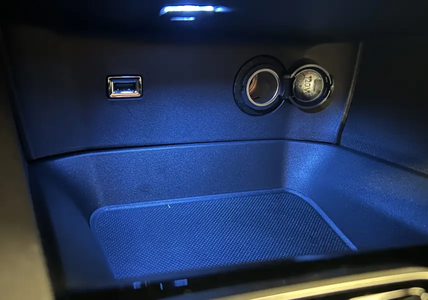 Prise USB et allume-cigare éclairés en bleu dans le compartiment central d’un Peugeot 5008 2024.