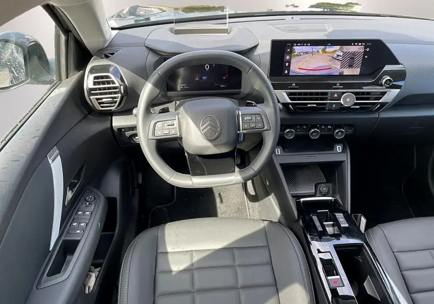 Vue intérieure avant centrée sur le volant cuir et l'écran tactile affichant la caméra de recul du Citroën C4 X noir 2025.