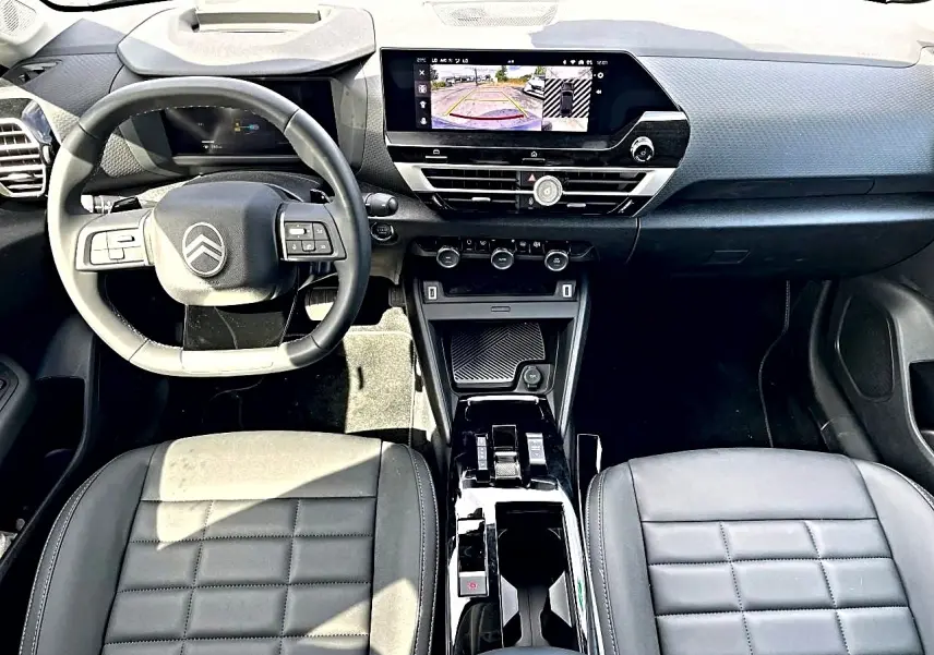 Vue intérieure avant du tableau de bord et volant cuir noir du Citroën C4 X 1.2 hybride avec écran tactile et caméra de recul affichée.