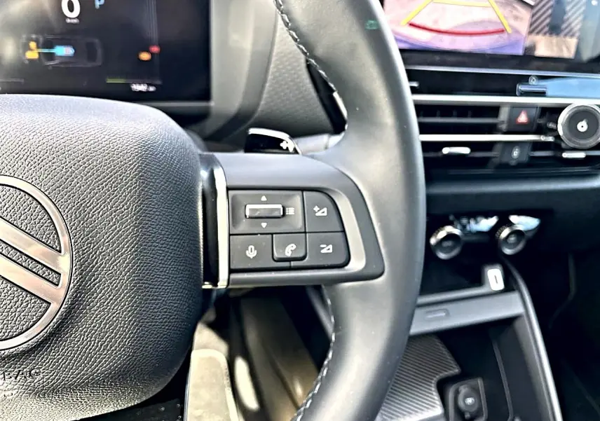 Vue rapprochée du volant cuir noir de la Citroën C4 X 2025 avec commandes vocales et écran tactile en arrière-plan.