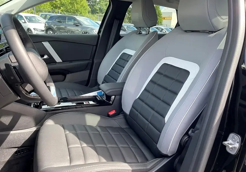 Vue intérieure côté conducteur de la Citroën C4 X noire 2025, sièges bi-matière gris et noir avec accoudoir central.