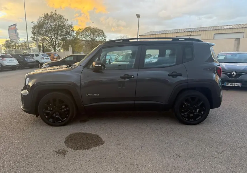 Profil côté droit d'un Jeep Renegade gris anthracite 2024 avec jantes alliage noires et barres de toit visibles.