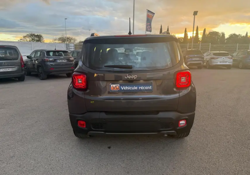 Vue arrière d'un Jeep Renegade gris anthracite 2024 avec feux arrière allumés et barres de toit visibles au coucher du soleil.