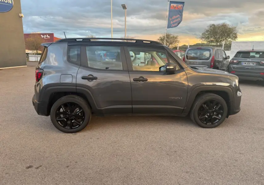 Jeep Renegade gris anthracite vue de profil côté gauche, avec jantes alliage noires et barres de toit visibles.