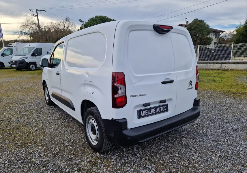 Vue 3/4 arrière droite d’un utilitaire Citroën Berlingo blanc, avec portes arrière fermées sur un sol gravillonné.