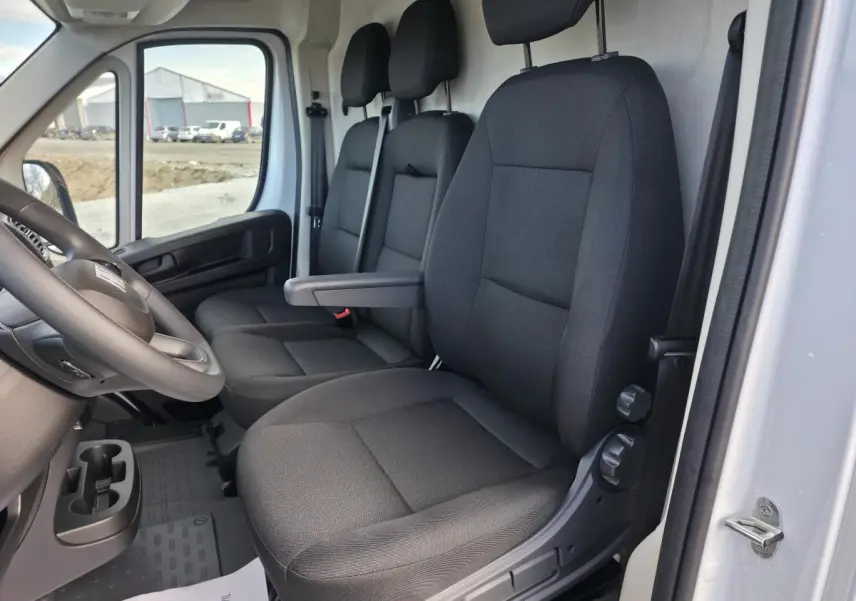 Vue intérieure côté conducteur du Fiat Ducato Fourgon blanc 2025, montrant les sièges en tissu noir et le volant.
