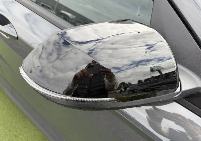 Rétroviseur droit noir brillant du Hyundai Kona II 1.6 Hybrid 138 N Line en Ecotronic Grey, reflet du ciel nuageux visible.