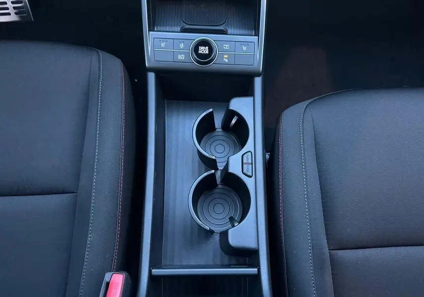 Vue plongeante sur la console centrale noire du Hyundai Kona 2026 avec porte-gobelets et commandes Drive Mode.