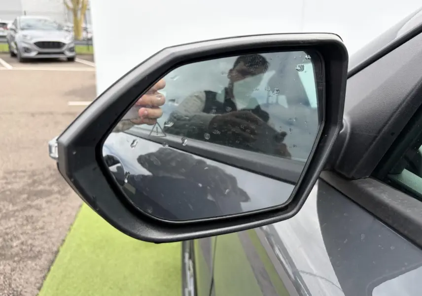 Rétroviseur extérieur côté gauche du Hyundai Kona 2026 en gris métallisé Ecotronic, avec reflet et gouttes d'eau visibles.