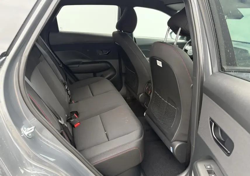 Vue intérieure arrière côté gauche du Hyundai KONA 2026 gris Ecotronic avec sièges tissu noir et surpiqûres rouges.