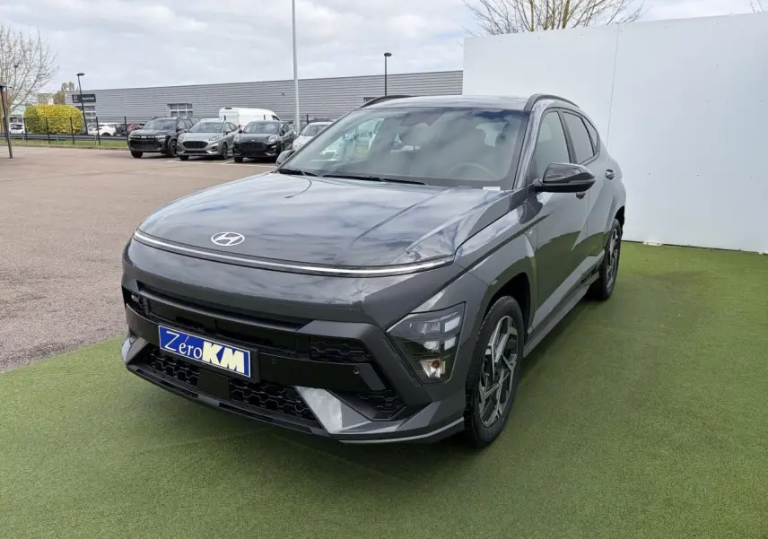 Hyundai Kona II 1.6 Hybrid N Line gris Ecotronic en 3/4 avant droit sur sol vert avec calandre noire distinctive.