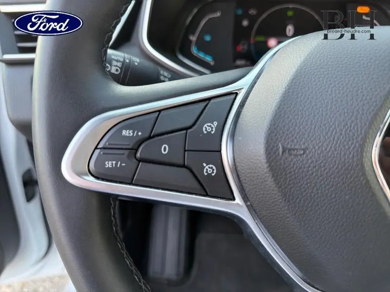 Gros plan sur les commandes de régulateur de vitesse au volant d'une Renault Clio blanche, intérieur noir.