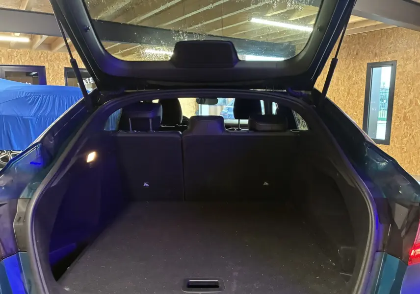 Coffre ouvert vu de l'arrière d'un Renault Arkana bleu, montrant l'espace de chargement intérieur vide.