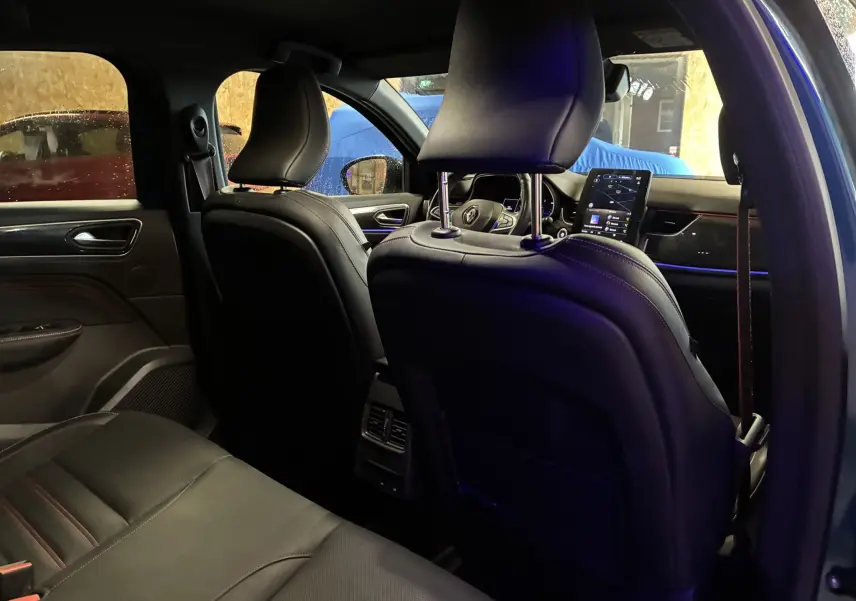 Vue intérieure arrière côté gauche du Renault Arkana bleu 2021, mettant en valeur les sièges en cuir noir et l'écran tactile central.