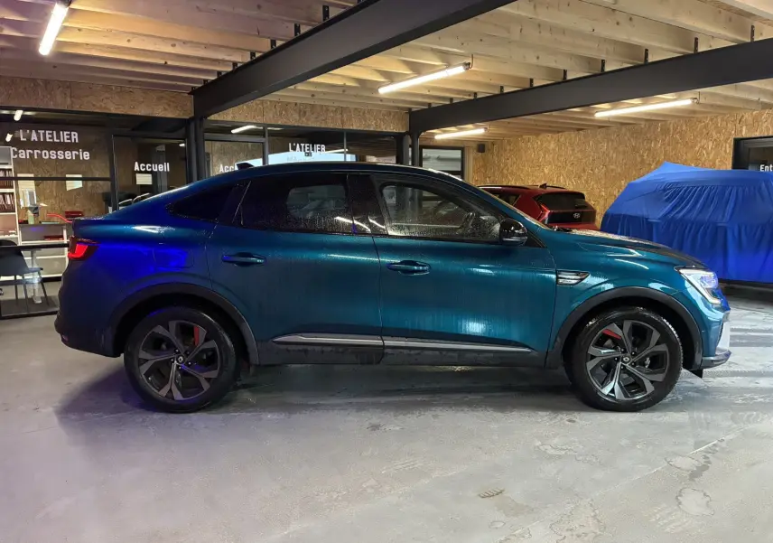 Vue de profil côté gauche d'un Renault Arkana bleu 1.3 TCE 140 RS-LINE avec jantes noires et étriers rouges, en intérieur.