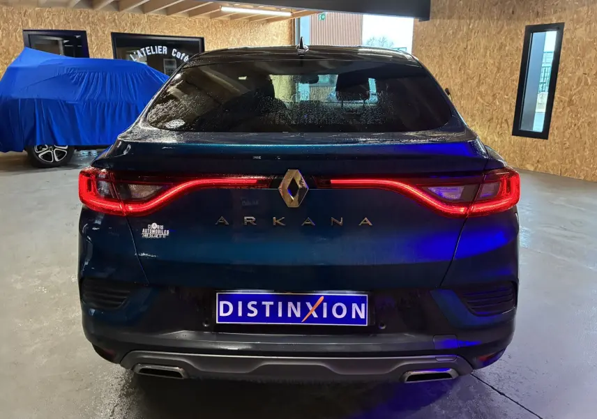 Vue arrière d'un Renault Arkana bleu 2021 avec feux LED allumés et double sortie d'échappement dans un garage.