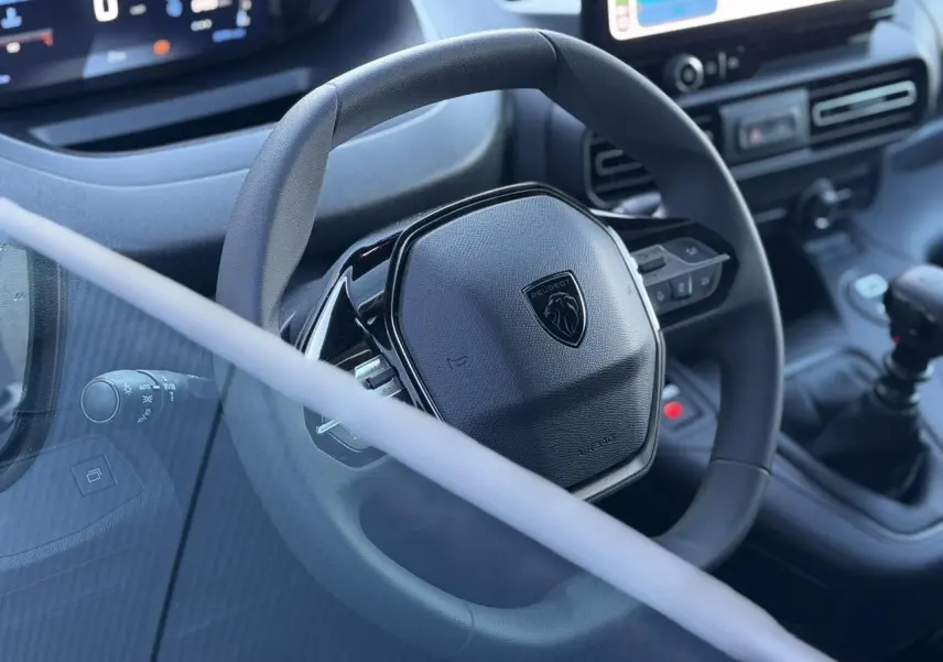Vue rapprochée du volant noir Peugeot Partner 2026 avec tableau de bord et levier de vitesses manuelle.