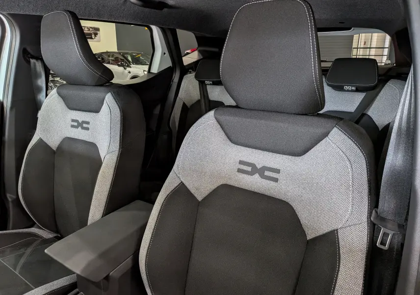 Vue rapprochée des sièges avant gris et noirs du Dacia Duster Hybrid-G 150 CH 4x4, avec logo distinctif brodé.