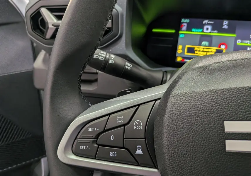 Gros plan sur le volant côté gauche du Dacia Duster blanc Glacier 2026, avec commandes de régulateur et tableau de bord numérique.