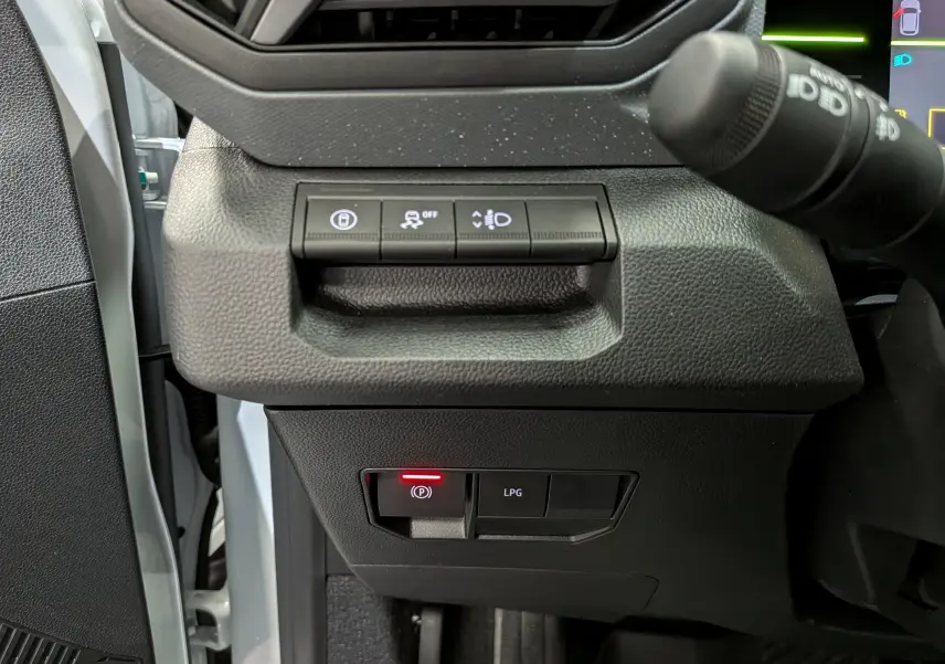 Détail intérieur côté gauche du tableau de bord du Dacia Duster blanc Glacier, avec commandes électroniques et bouton GPL.