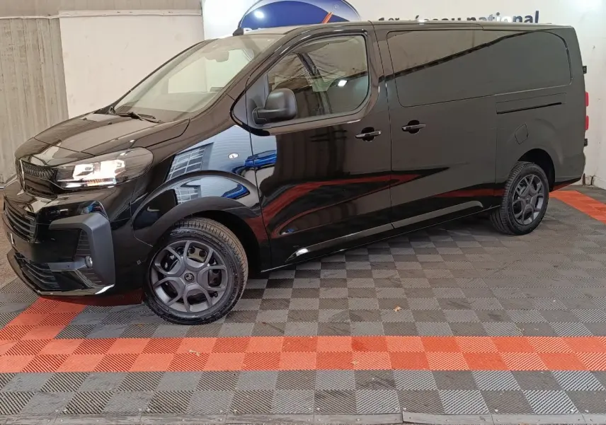 Vue 3/4 avant gauche d’un Citroën Jumpy XL noir avec phares allumés et jantes noires, stationné en intérieur.