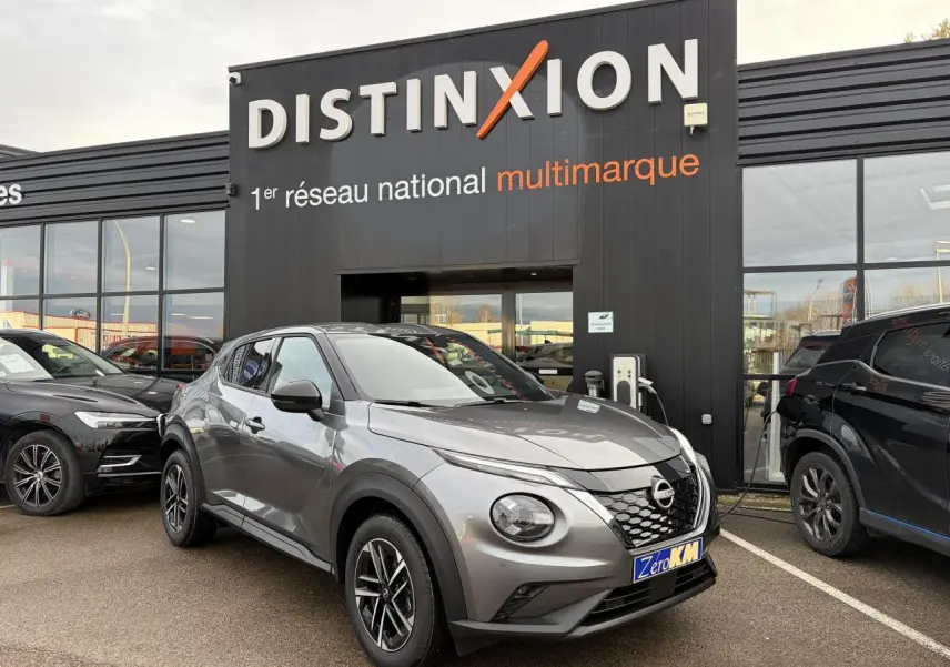 Nissan Juke II 1.6 Hybrid noir métal en 3/4 avant droit, avec jantes alliage et calandre distinctive, devant un showroom.