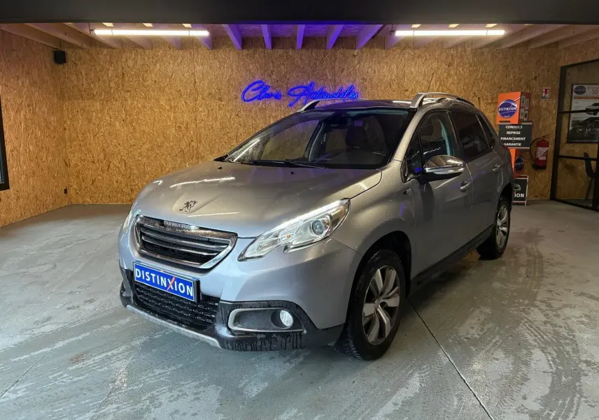 Peugeot 2008 gris vue 3/4 avant droit dans un garage, avec toit ouvrant et jantes alliage visibles.