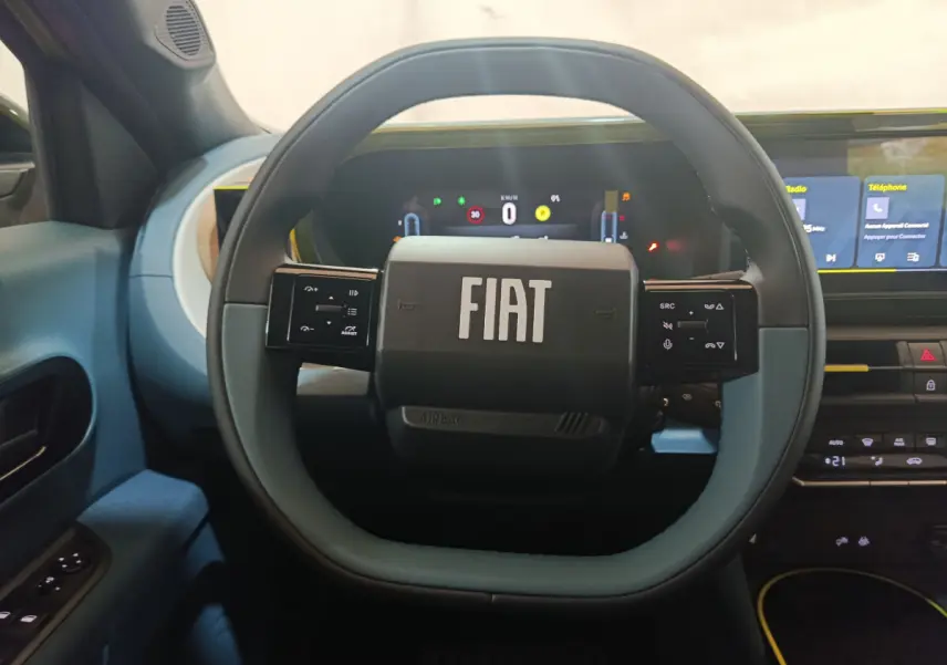 Vue intérieure centrée sur le volant bleu clair de la Fiat Grande Panda 2025 avec tableau de bord numérique et écran tactile.
