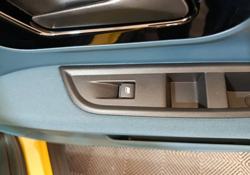 Détail de la commande de vitre sur la porte côté conducteur d’une FIAT Grande Panda jaune avec habillage bleu.