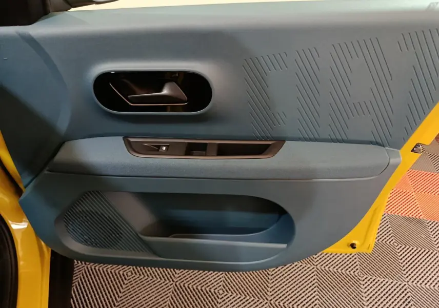 Vue intérieure côté gauche de la porte avant jaune de la FIAT Grande Panda avec garniture bleue et poignée noire.