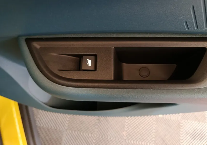 Gros plan sur la commande de lève-vitre côté conducteur d'une Fiat Grande Panda jaune, intérieur bleu-gris.