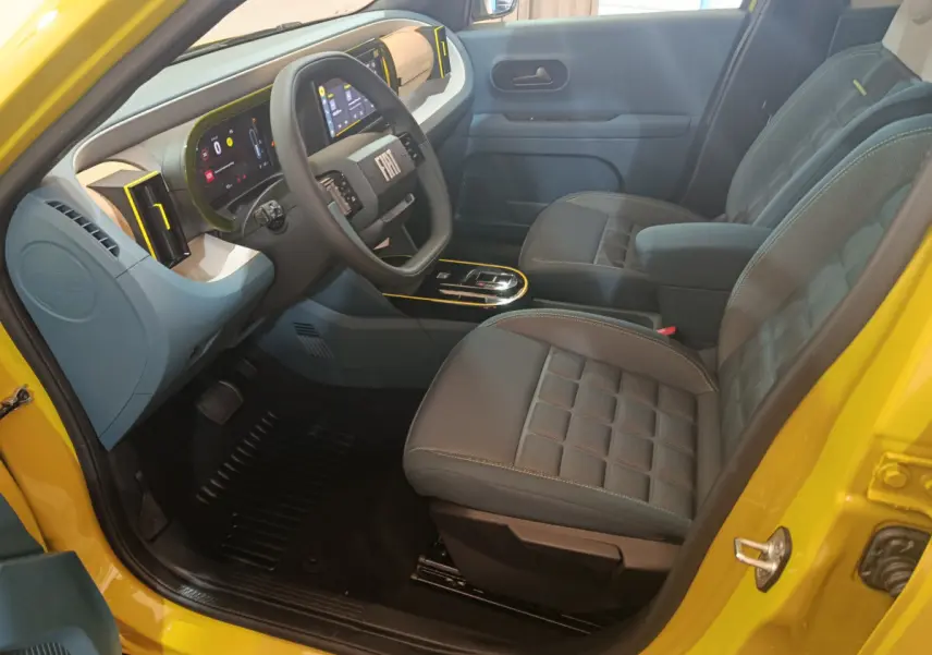 Intérieur avant droit de la FIAT Grande Panda jaune 2025, volant cuir, tableau de bord digital et sièges gris matelassés.