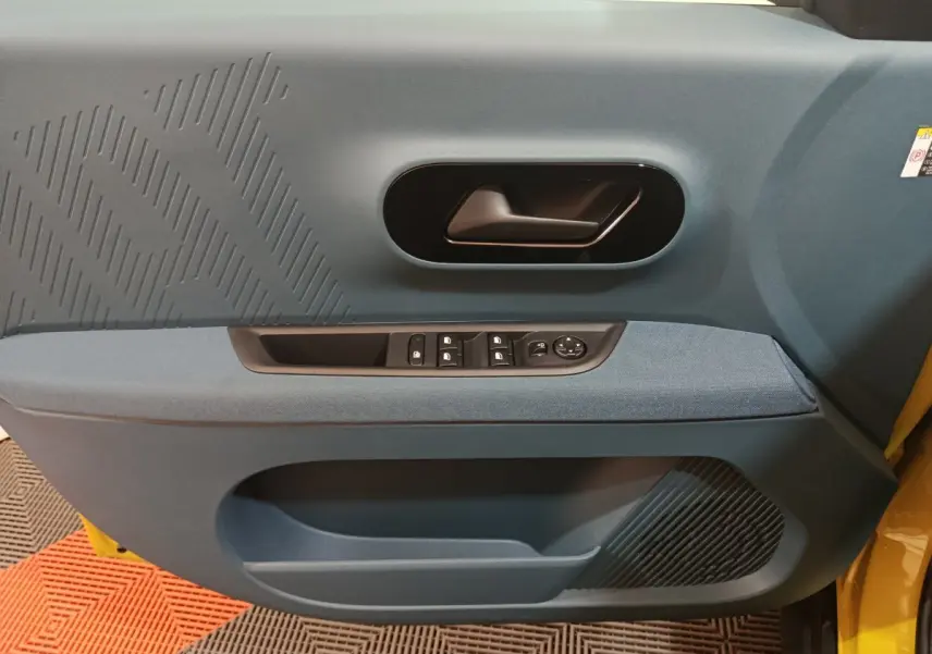 Vue intérieure côté gauche de la porte avant d’une FIAT Grande Panda jaune avec garniture bleue et commandes électriques.