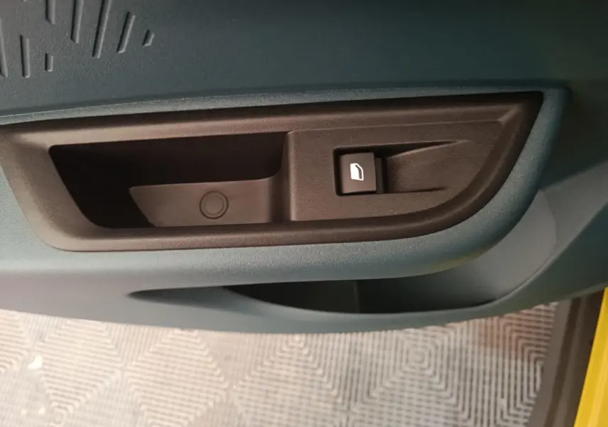 Détail de la poignée intérieure de porte noire sur fond bleu de la FIAT Grande Panda jaune 2025, côté conducteur.