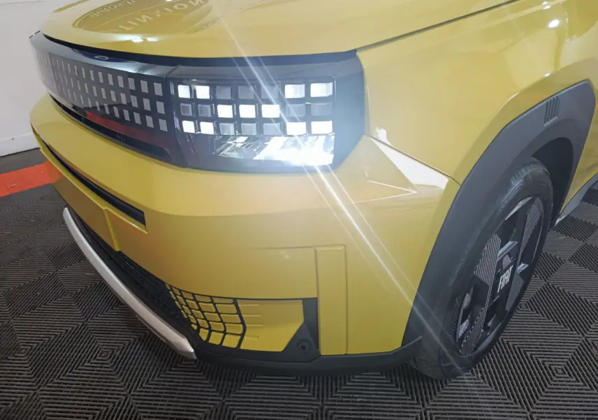 Gros plan sur l'avant droit jaune vif de la FIAT Grande Panda 2025 avec phares LED allumés et jante noire distinctive.