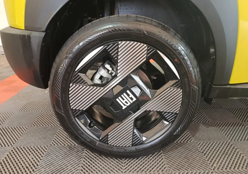 Gros plan sur la roue avant gauche de la FIAT Grande Panda jaune, mettant en valeur la jante noire et argentée au design géométrique.