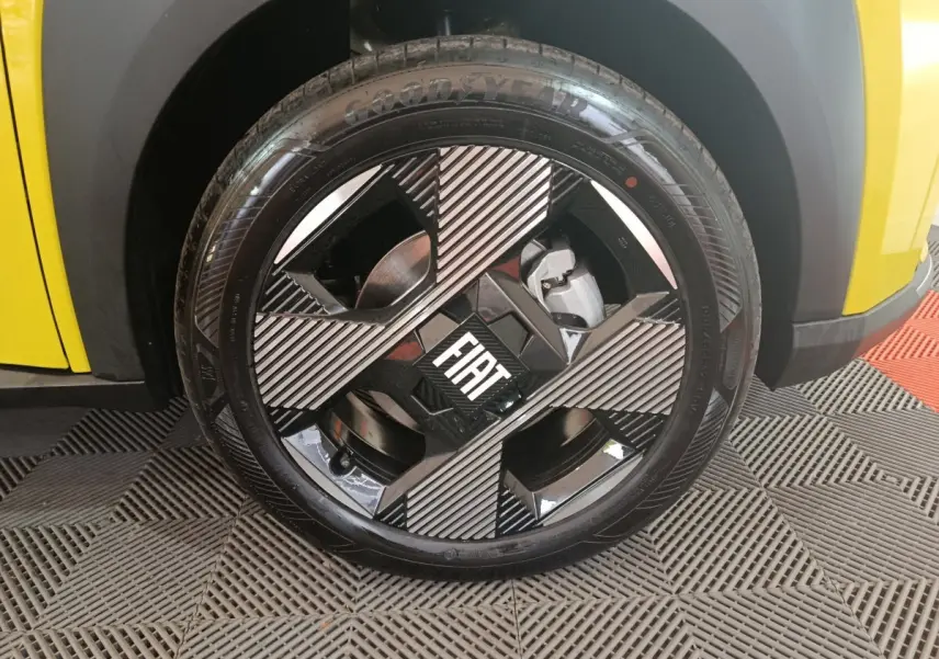 Gros plan sur la roue avant gauche jaune de la Fiat Grande Panda avec jante noire et grise au logo FIAT central.