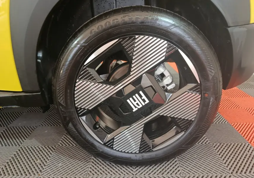 Gros plan sur la roue avant droite d’une FIAT Grande Panda jaune, jante noire et argent au design géométrique.