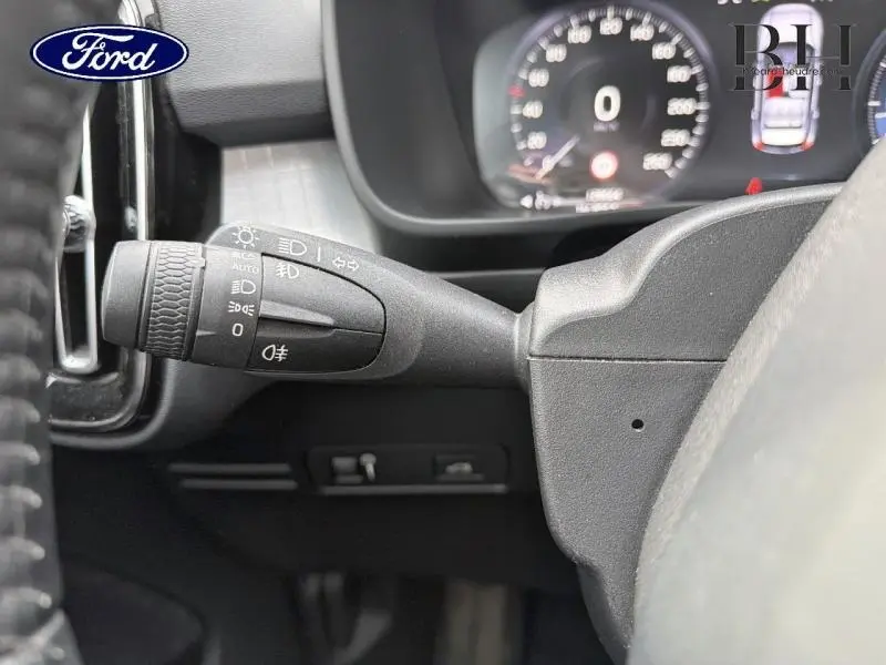 Gros plan sur la manette des phares et clignotants à gauche du volant dans l'habitacle d'un Volvo XC40 blanc.