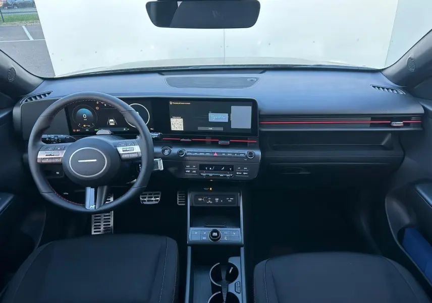 Intérieur avant du Hyundai Kona 2025 noir Abyss, tableau de bord numérique et écran tactile large avec touches rouges décoratives.