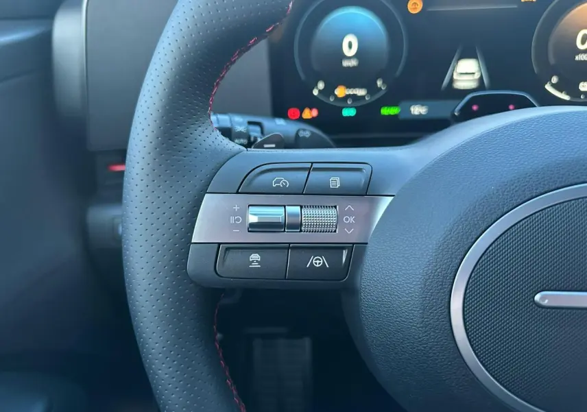 Gros plan sur les commandes gauche du volant cuir perforé du Hyundai KONA 2025, affichage numérique en arrière-plan.
