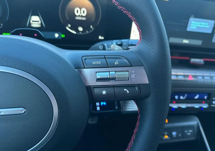 Gros plan sur le volant cuir noir avec surpiqûres rouges et commandes multifonctions du Hyundai Kona 2025.