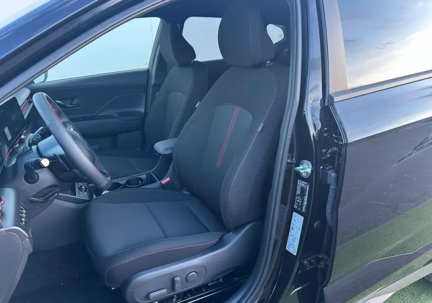 Vue intérieure côté gauche du Hyundai KONA 2025 noir Abyss Metal, sièges avant N Line avec surpiqûres rouges et volant cuir.