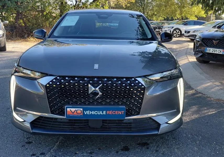 Vue frontale d'une DS4 hybride gris métallisé avec calandre noire à motifs losanges et feux diurnes verticaux allumés.