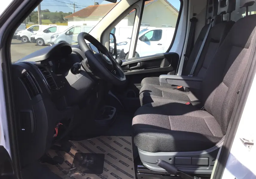 Intérieur côté conducteur du FIAT Ducato Chassis Benne blanc 2023, sièges tissu noir et volant multifonction.