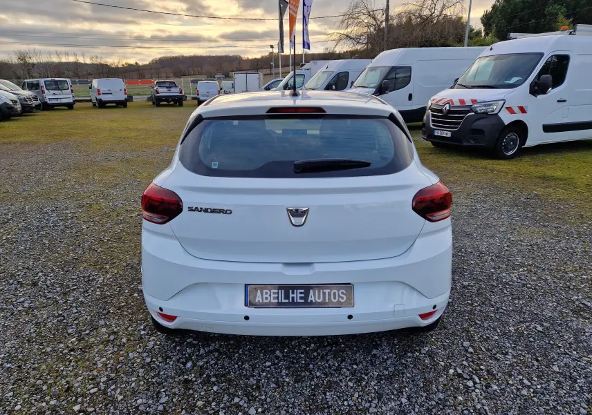 Vue arrière d'une Dacia Sandero blanche 2022, avec feux rouges et plaque Abeilhe Autos sur un parking extérieur.