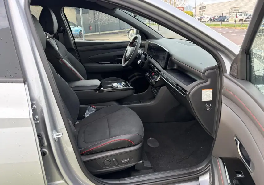 Vue intérieure côté conducteur du Hyundai Tucson 2025 en Shimmering Silver, sièges cuir/alcantara noirs avec surpiqûres rouges.